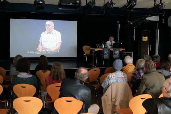 Brigitte am Tisch auf der EWH-Bühne zeigt Beispiel aus der Ausstellung